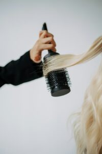 A woman studies her hair in the bathroom mirror, holding a bottle of clarifying shampoo in one hand.