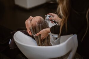 A woman gently brushes her hair in natural light, focusing on her scalp and healthy hair care routine.