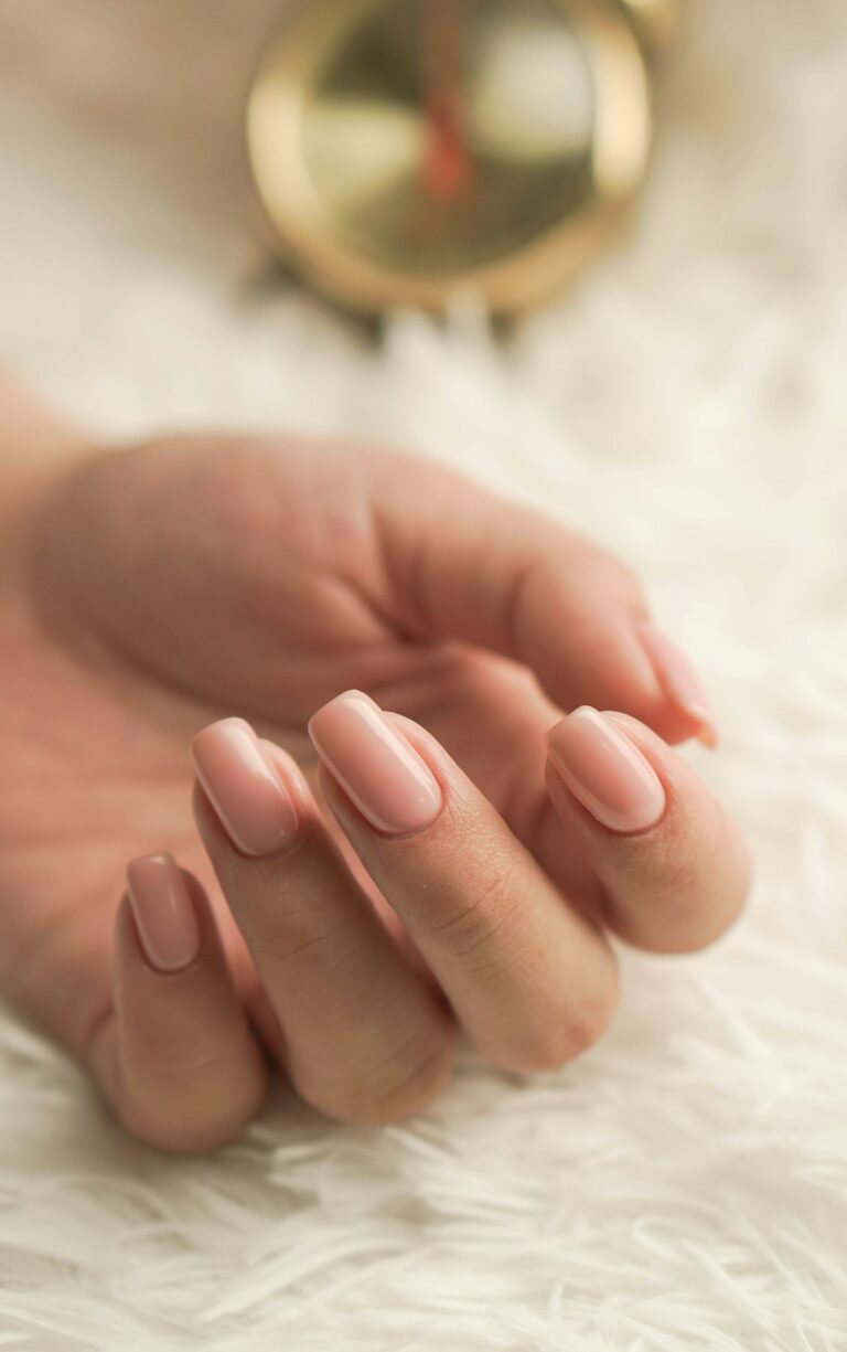 A close-up of a hand displaying gel, acrylic, and dip powder nails in different colors for comparison.